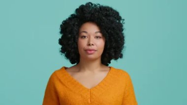 20 'li yaşlarda, turuncu kazaklı genç Afro-Amerikalı bir kadın kameraya bakar, dua ederken el ele tutuşur, iyi bir şey için yalvarır, stüdyoda mavi arka planda bir şey ister. Halkın yaşam tarzı konsepti 4K