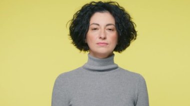 Sakin, sinirli, olgun bir kadın boynu kesilmiş, sarı arka plan. Yetişkin bir kadın kameraya bakıyor. Elle boğaz kesmekle tehdit ediyor. İntikam saldırganlığının jestini gösteriyor.