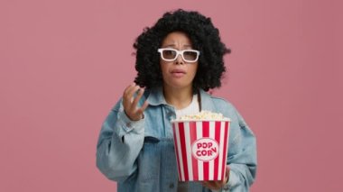 Neşeli Afro-Amerikalı kadın spor maçı sonuçlarını izlerken çığlık atıyor ve izole edilmiş pembe stüdyo arka planında patlamış mısır yiyor. Süper heyecanlı tutkulu siyah kadın fanatik takım kazandığında çığlık atıyor