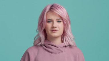 Pembe saçlı öğrenci kızın portresi birden boynu ağrımaya başladı. Renkli saç stili boynu ağrıyan yorgun genç bir kadın. Stüdyo mavi arka planda çekilen sağlık ve tıbbi konsept 4K