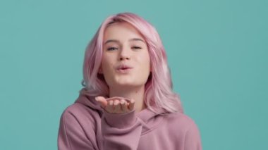 Pastel mavisi stüdyo arka planında pembe saçlı güzel hippi kızın hava öpücüğüyle hoşça kal jesti. Pembe saçlı mutlu bayan seni avucunun içinden yavaşça öper.