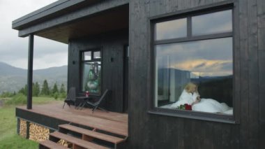 Etrafı dağlık manzaralı, modern, kırsal bir kır evi. Beyaz battaniyeye sarılmış, sabah kahvesini yudumlayan bir kadın. Yüksek kalite 4k görüntü