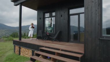 Beyaz bornozlu güzel, beyaz bir kadın, savurgan kırmızı güller kokluyor. Sarışın bayan glamping tarzında sakin bir tatilin tadını çıkarıyor. Yüksek kalite 4k görüntü