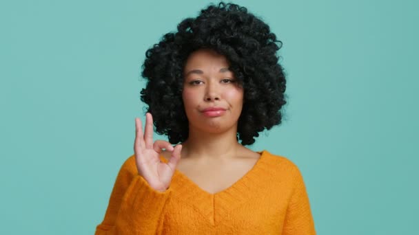 巻き毛の美しいアフリカ系アメリカ人女性は 青の背景で指でOkのサインを懐疑的に示しています 黒人女性が不本意ながら何かに同意する肖像 — ストック動画