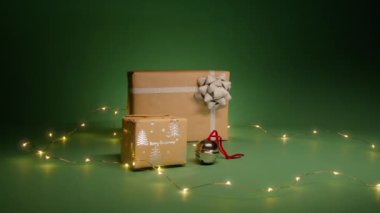Kraft kağıdına sarılı hediye kutuları ve Noel Geyiği çanı. İzole edilmiş zümrüt yeşili arka planda geceleri fotokopi alanı olan Noel süslemeleri. Parlayan çelenk Noel ruhu yayıyor.