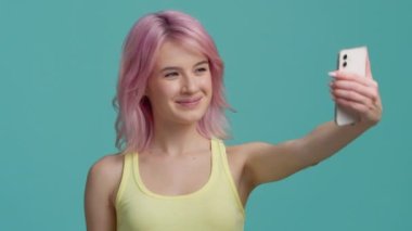 Pastel arka planda pembe saçlı genç bir kadın. Milenyum seyahat blogcusu akıllı telefondan hava öpücüğü yolluyor. Sosyal medya ya da anılar için video yap. Yeni nesil konsept stüdyosu