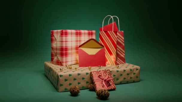 クリスマスグリーティングカードの中に赤い封筒と黄金の色を開いた 愛と家族のコンセプトショットスローモーションエメラルドグリーンの動きの背景にプレゼントを形成する赤いクリスマスギフトボックスのスタック — ストック動画