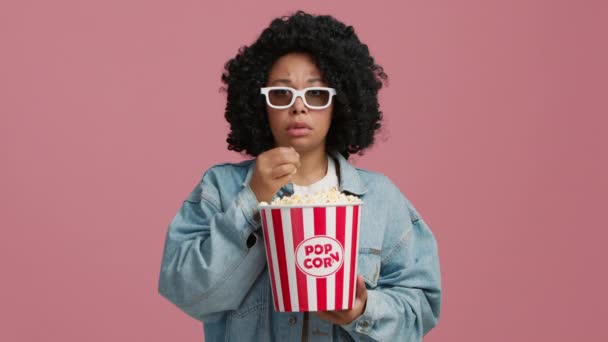 動揺したアフリカ系アメリカ人女性がテレビで3Dドキュメンタリー映画を注意深く見ているのを心配している姿を 女性は自分が見たものを信じないまま3Dメガネを下げている ポップコーンを制御不能に食べる — ストック動画