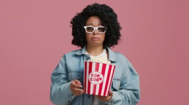 Televizyonda romantik drama filmi izlerken ağlayan Afrikalı Amerikalı kadının portresi. Duygusal empatik kadın göz yaşlarını silmek için 3D gözlüklerini çıkarıyor. Kontrolsüz bir şekilde patlamış mısır yemek.