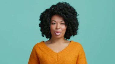 Oyuncu Afro-Amerikan model doğrudan kameraya bakıyor ve dil gösteriyor, sonra da beyaz sağlıklı dişlerle gülüyor. Gerçek insan konsepti, siyah kıvırcık saçlı, koyu tenli farklı model.