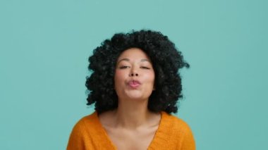 Komik Afro-Amerikan model kameraya doğru bakıyor ve hava öpücüğü veriyor, güzel beyaz dişleriyle gülümsüyor ve utanç içinde gözlerini indiriyor. Kıvırcık saçlı utangaç manken.