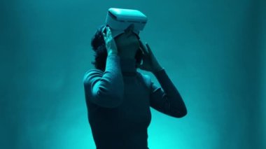 Olgun bir kadın sihirli mavi ışık atmosferinde sanal ya da artırılmış gerçeklik gözlüğü kullanır. Dijital etkileşimli performansta VR kulaklık kullanıcısı olan kadın modeli, geleceğin eğlencesi, teknoloji