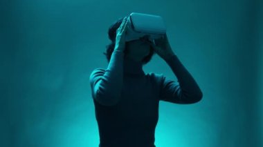 Dijital etkileşimli performansta VR kulaklık kullanıcısı olan kadın model, geleceğin eğlencesi, teknoloji. Olgun bir kadın sihirli mavi ışık atmosferinde sanal ya da artırılmış gerçeklik gözlüğü kullanır.