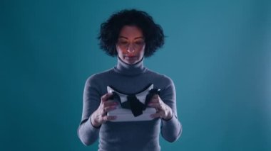 VR fütüristik eğlence konsepti 4K. Sanal gerçeklik kulaklığı kullanan ve interaktif teknoloji AR 'ı renkli ışıklandırmalı, mavi arka planda yavaş çekim yapan heyecanlı olgun bir kadın.