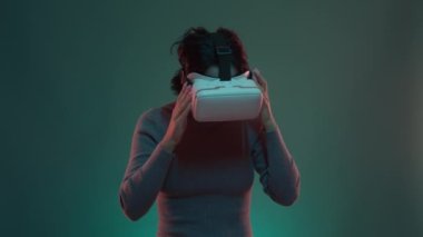 Neon VR oyuncusu, gülümseyen yetişkin bir kadın. Sanal gerçeklik stüdyosundaki mutlu insanlar, simülasyon gözlüğü teknolojisi. VR cihazında gözlüklü bir kumarbaz. AR teknolojisini kullanan insanlar. Yeşil mavi ışık 4K