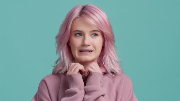 有趣的肖像吓到了20多岁的年轻漂亮嬉皮士学生 在孤立的蓝色工作室背景4K上 带着淡淡的粉色头发的帽衫 紧张的年轻女人感到恐慌 担心和困惑 — 图库视频影像