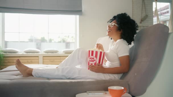 坐在客厅沙发上 吃爆米花点心 看喜剧电视节目 慢动作的美丽的笑着大声说出来的非洲裔美国女人 周末在时尚住宅内的闲暇时间4K — 图库视频影像