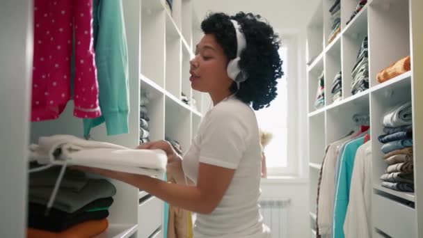 美丽时尚的非洲裔美国女人的肖像 一边整理衣橱一边用耳机听音乐 贞洁的女佣在衣柜里做春季清洁 服务人员4K — 图库视频影像