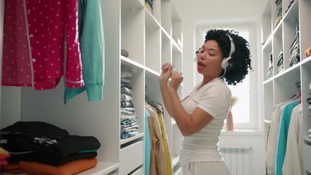 非洲裔美国女人的画像 一边在耳机里听音乐一边玩乐和跳舞 整理衣橱 少女在衣柜里散步 做春季清洁 服务人员 — 图库视频影像