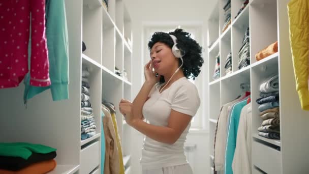 少女在衣柜里散步 做春季清洁 服务人员 非洲裔美国妇女的画像 一边在耳机里听音乐一边玩乐和跳舞 整理衣橱 — 图库视频影像