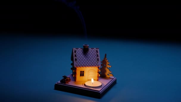 煙突から煙が出てくる小さな木造ログハウスおもちゃと建物の前で燃えるティーキャンドルと魔法の夜の背景 クリスマスの夜の背景とともにコピースペースでスローモーションRed — ストック動画