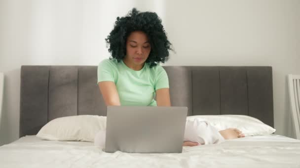 幸せなヒップスターGen Zアフリカ系アメリカ人女性学生とともにアフロヘア使用ラップトップコンピュータ 上に座っているベッドルームでスタイリッシュな自宅 ホテル 遠隔学習 ラーニングやインターネットでの作業 — ストック動画