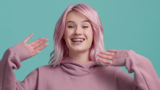 ピンクの髪を持つ若い幸せなヒップスターVloggerの女の子は 孤立した背景スタジオでカメラに話してウェブカメラを見て手を振っています 仮想チャット会議でのスローモーションモデルの呼び出し 社会的距離の友人 — ストック動画