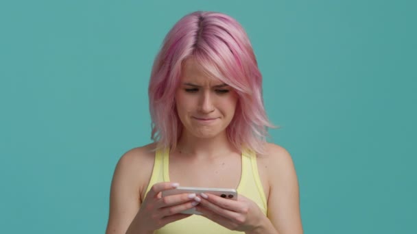 ピンクの髪をした若い十代のヒップスターの女の子は 友人や家族からの良いニュースで電子メールやテキストを受信します 教育やソーシャルメディアアプリについて スローモーション笑顔の顔に隔離された青の背景 — ストック動画