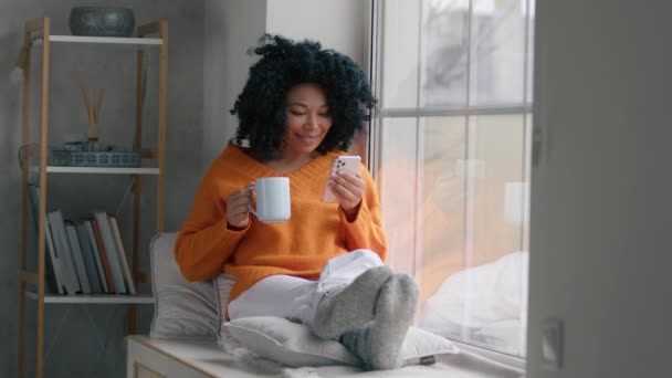 拥有一头卷曲黑发的女性博主在手机上订阅新的社交媒体 购买互联网 在线订购应用程序产品 在家里使用智能手机的快乐非洲裔美国人模式 — 图库视频影像