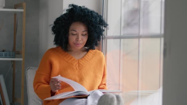 Кінематограф Молодої Афроамериканської Жінки Яка Читає Книжку Насолоджуючись Вікном Вітальні — стокове відео