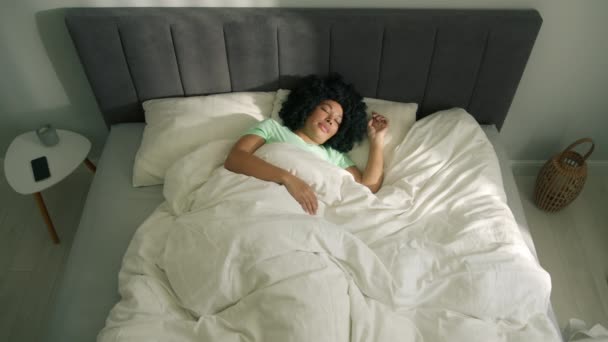 柔らかい枕の白いリネン整形外科のマットレスの快適な居心地の良い新鮮なベッドでよく眠る穏やかな若いアフリカ系アメリカ人女性 穏やかな女の子寝そべって眠る朝の良い睡眠を楽しんで — ストック動画