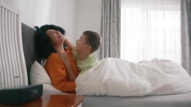 Gülümseyen melez bir anne ve yatak odasında sarılan sevimli bir çocuk. Anne ve çocuğun hassas anlarında eğlence zamanı yavaşlar. Afro-Amerikan anneyi seven, sarılan, tatlı tatlı çocuk yatakta uzanan.