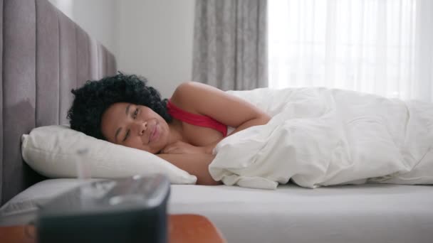 若い幸せな美しいアフリカ系アメリカ人女性の肖像カメラの前でベッドの早朝に目が覚めた後に横たわって笑顔 可愛い色の女性は枕の上のベッドルームで幸せそうに見えます4K — ストック動画