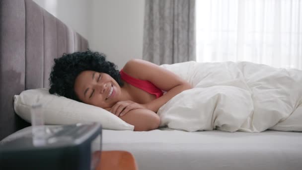 色のかわいい美しい女性は 枕4Kの寝室で幸せに見えます 若い幸せな美しいアフリカ系アメリカ人女性の肖像カメラの前で笑顔目が覚めた後 早朝にベッドに横たわっていた — ストック動画