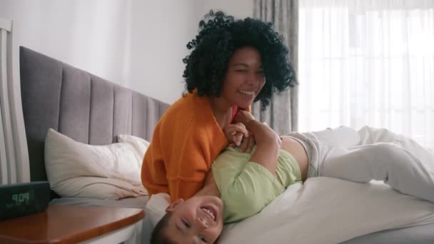 アフリカ系アメリカ人のママがベッドの上に寝そべっている 笑顔思いやりのある混合レースの母親とかわいい小さな子供がベッドルームで抱っこ ママと子供の優しい瞬間楽しい時間遅い — ストック動画
