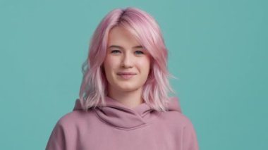 Genç oyuncu hippi kadın kameraya bakarak flört ediyor. Piercingli ve diş telli bir portre kızı. Yavaş çekim kapak havalı funky kız moda pembe saç rengi dil gösteren
