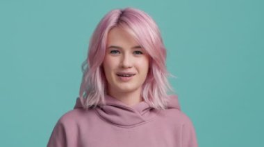 Yavaş çekimde moda pastel pembe saç rengi dil gösteren havalı funky kızı kapat. Genç oyuncu hippi kadın kameraya bakarak flört ediyor. Piercingli ve diş telli bir portre kızı.