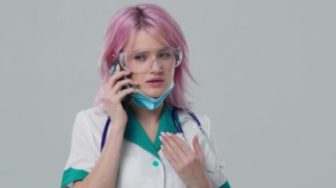 Tıbbi terapist asistanı konferansında. Portre görüntüsü. Teletıp salgını konsepti 4K. Koruyucu gözlük takan çekici genç bayan doktor cep telefonuyla hastaya danışmanlık yapıyor.
