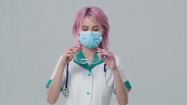 RSV ya da Covid19 salgını yavaş çekim 4K çekimi. İzole bir zeminde duran gülümseyen Kafkas terapist kadın doktor. Kendine güvenen hemşire baca boşluğunda koruyucu yüz maskesi takıyor.