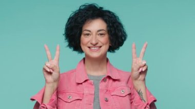 Kısa siyah kıvırcık saçlı, güzel, olgun bir kadın. İki elinde de V zafer işareti var. Güzel 40 'lı yaşlarda bir kadın mavi stüdyo arka planında ağır çekimde kazanan jestler sergiliyor.