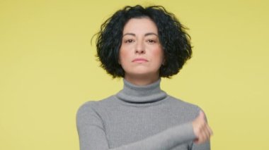 Yetişkin bir kadın, kameraya bakıp, intikam saldırganlığı gösterisiyle boğaz kesmekle tehdit ediyor. Stüdyo 4K çekti. Sakin, sinirli, olgun bir bayan boynu kesilmiş, sarı arka plan.