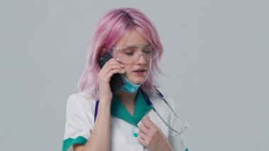 Teletıp. İnternetteki doktor randevusu 4K. Beyaz önlüklü, koruyucu Google ve steteskop kullanan akıllı dost canlısı kadın klinisyen hastane ofisinde uzaktan hasta danışmanlığı için cep telefonu kullanıyor.