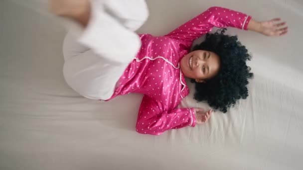 幸せなアフリカ系アメリカ人女性のベッドやソファの上でリラックスを楽しんで笑ってジャンプします 居心地の良いソファで休んで 週末や休日をお祝いしましょう 休日の朝を楽しむパジャマ姿の女 — ストック動画