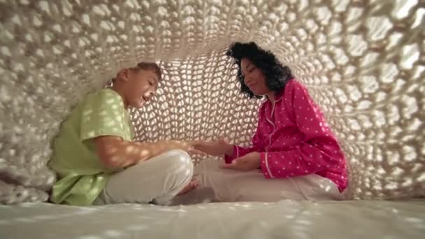 快乐的非洲裔美国母亲和小儿子坐在床上 被时尚舒适的针织毛毯覆盖着 电影般的晨光透过 色彩艳丽的女人和小孩一起玩石头剪刀 — 图库视频影像