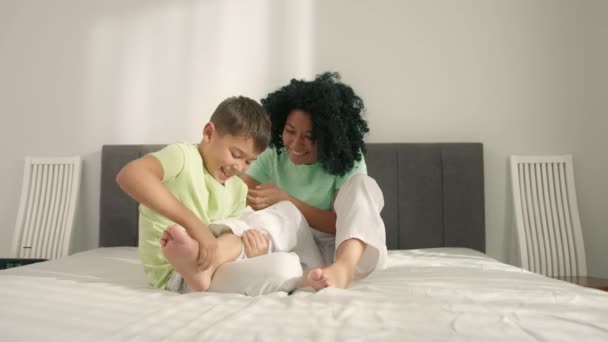 幸せな誠実な若いアフリカ系アメリカ人の母親は 愛らしい小さな就学前の息子と一緒に楽しんで大声で笑って 週末の朝に快適なベッドで一緒に遊んで 自宅でレジャーを楽しんでいます — ストック動画