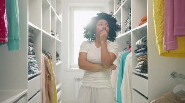 Ne giyeceğimi bilmiyorum, yardım et, elim kolum bağlı. Çaresiz Afro-Amerikalı kadın, kafası bir karış havada, raflara bakıyor. Renkli giysiler içinde, ne giyeceğini düşünüyor, zor kararlar vermeye çalışıyor.