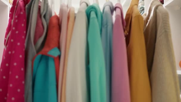 美丽而积极的非洲裔美国女人 卷曲的头发在扶手上把五颜六色的衣服分开 在购物中心买衣服的架子上笑着一个有色女人 促销服装店 — 图库视频影像