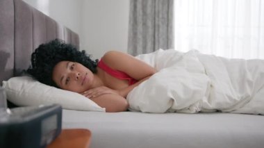 Depresyondaki genç Afrikalı Amerikalı kadın uykusuzluktan uyuyamıyor, ağır çekimde. Depresyondaki kadın uykusuzluktan muzdarip. Sabahın erken saatlerinde yatakta yatıyor. Ruh sağlığı konsepti görüntüsü 4K