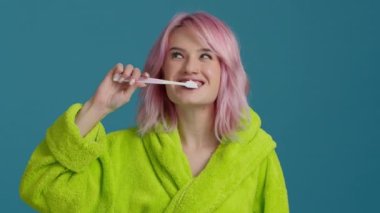 Yakın plan, pembe saçlı, diş fırçası ve diş macunuyla dişlerini fırçalayan mutlu bir kadın. Gülücükler saçan güzel kız sabah ağız temizliği önleyici sıhhi kıyafet banyoda yalnız başına 4K