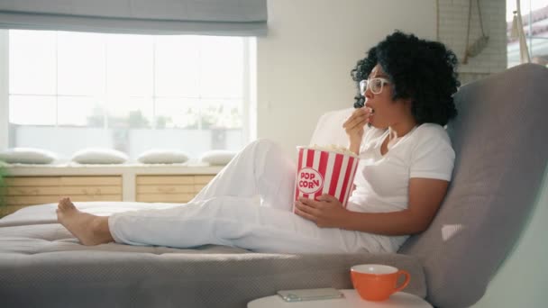 美国黑人女性在电视上看娱乐性电影 女性真的很害怕恐怖片情节和特效 迷人的女人坐在沙发上 家里提着爆米花篮 — 图库视频影像